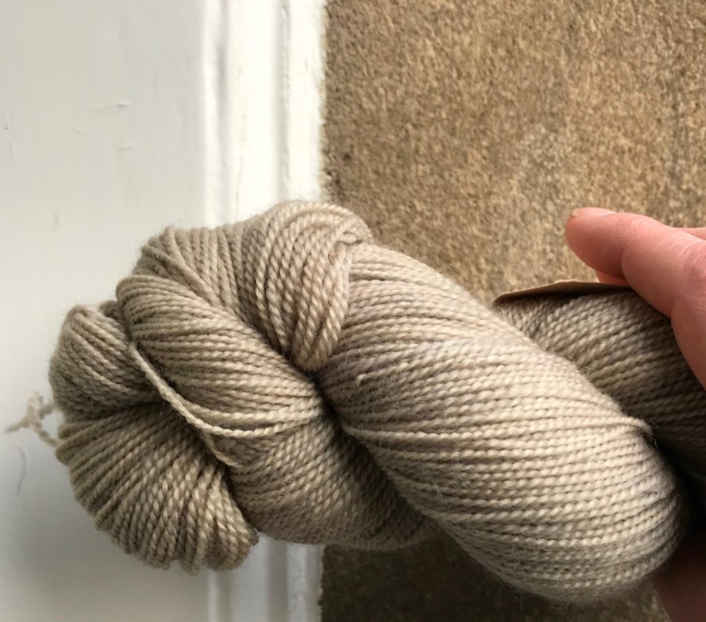Skein of greige yarn held against a wall of the same colourway.
