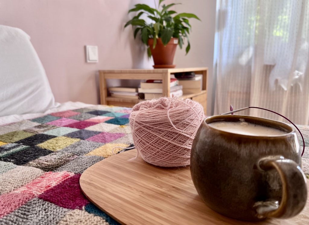 close up of cup sitting beneath a yarn cake on the bed that is covered with a memory blanket